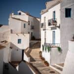 Calle empedrada con casas encaladas de estilo andaluz en Frigiliana, con detalles en azul en ventanas y balcones.