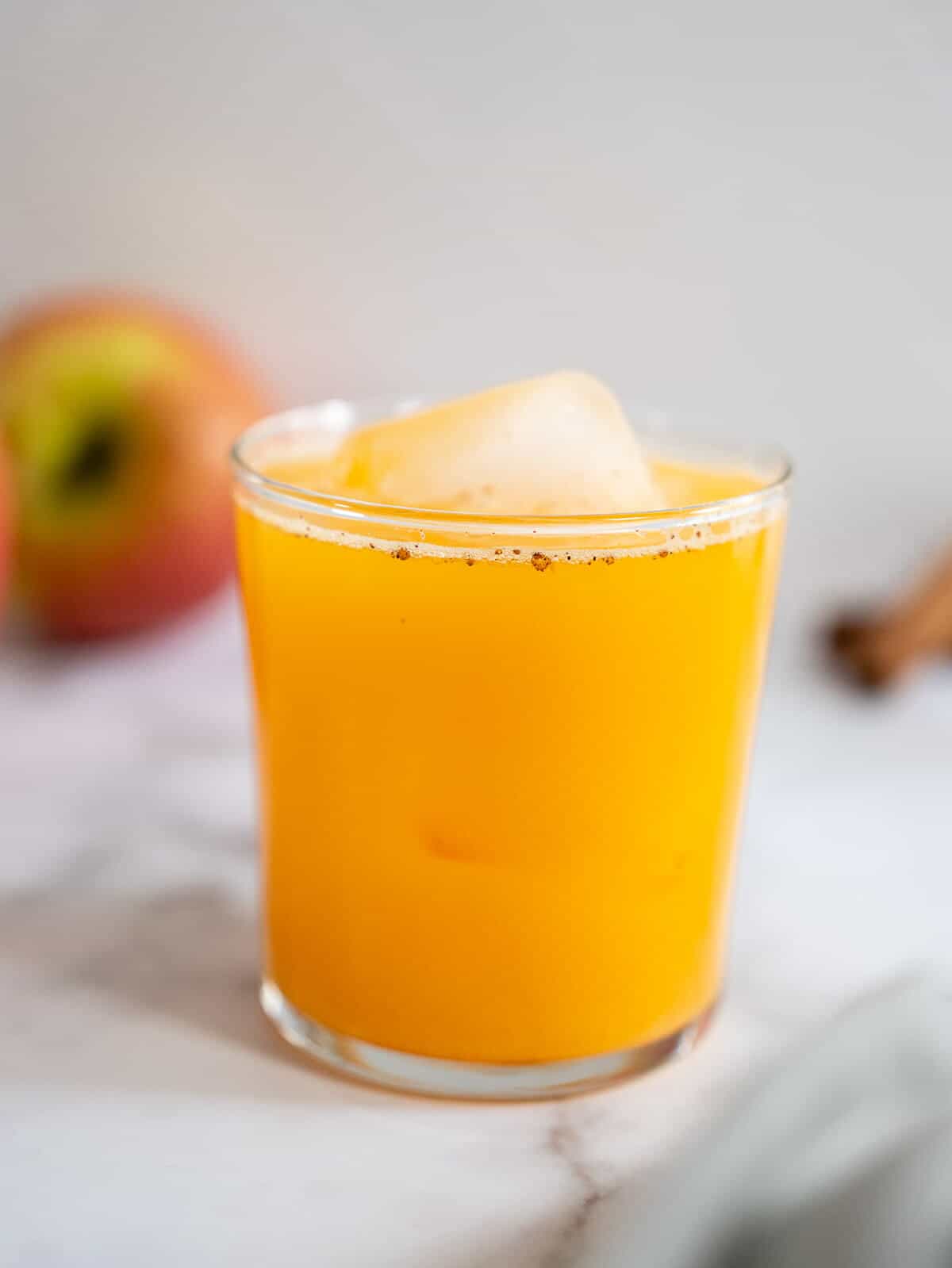 Jugo de calabaza y manzana en vaso con un cubo de hielo, mostrando su color vibrante y textura refrescante. Ideal para quienes buscan recetas naturales y saludables en 'Nómadas Gourmet.