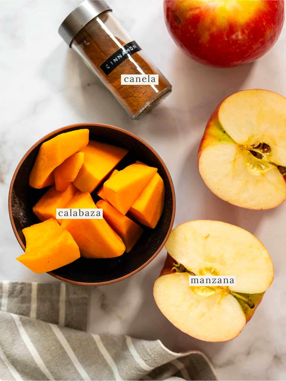 Ingredientes frescos para un jugo de calabaza gourmet: manzanas cortadas, trozos de calabaza y canela en polvo sobre una mesa de mármol. Perfecto para una receta otoñal saludable y deliciosa.