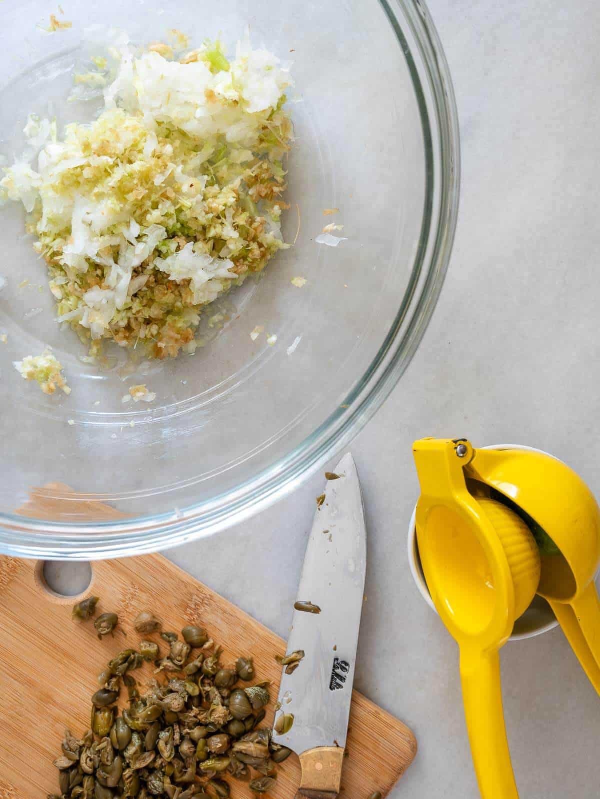 alcaparras picadas y exprimidor de limas amarillo sobre una tabla de cocina.