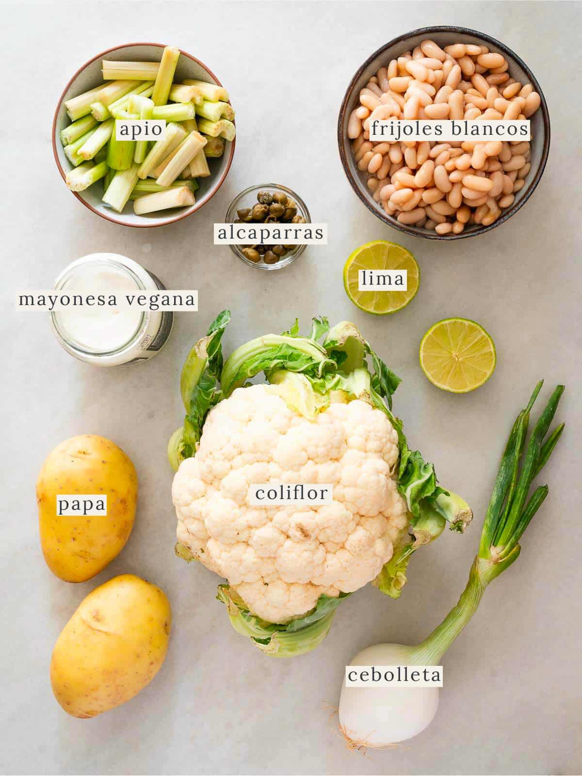 ingredientes frescos para ensalada vegana de coliflor y papas, incluyendo apio, alcaparras, frijoles blancos y cebolleta.