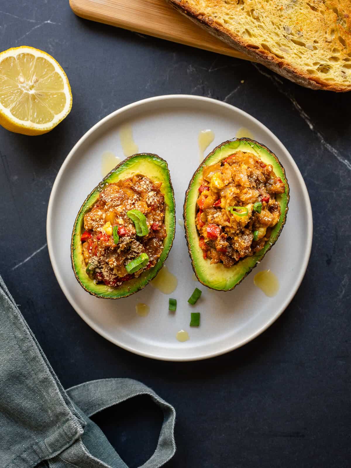 Dos mitades de aguacate relleno en un plato, acompañadas de pan tostado y limón.