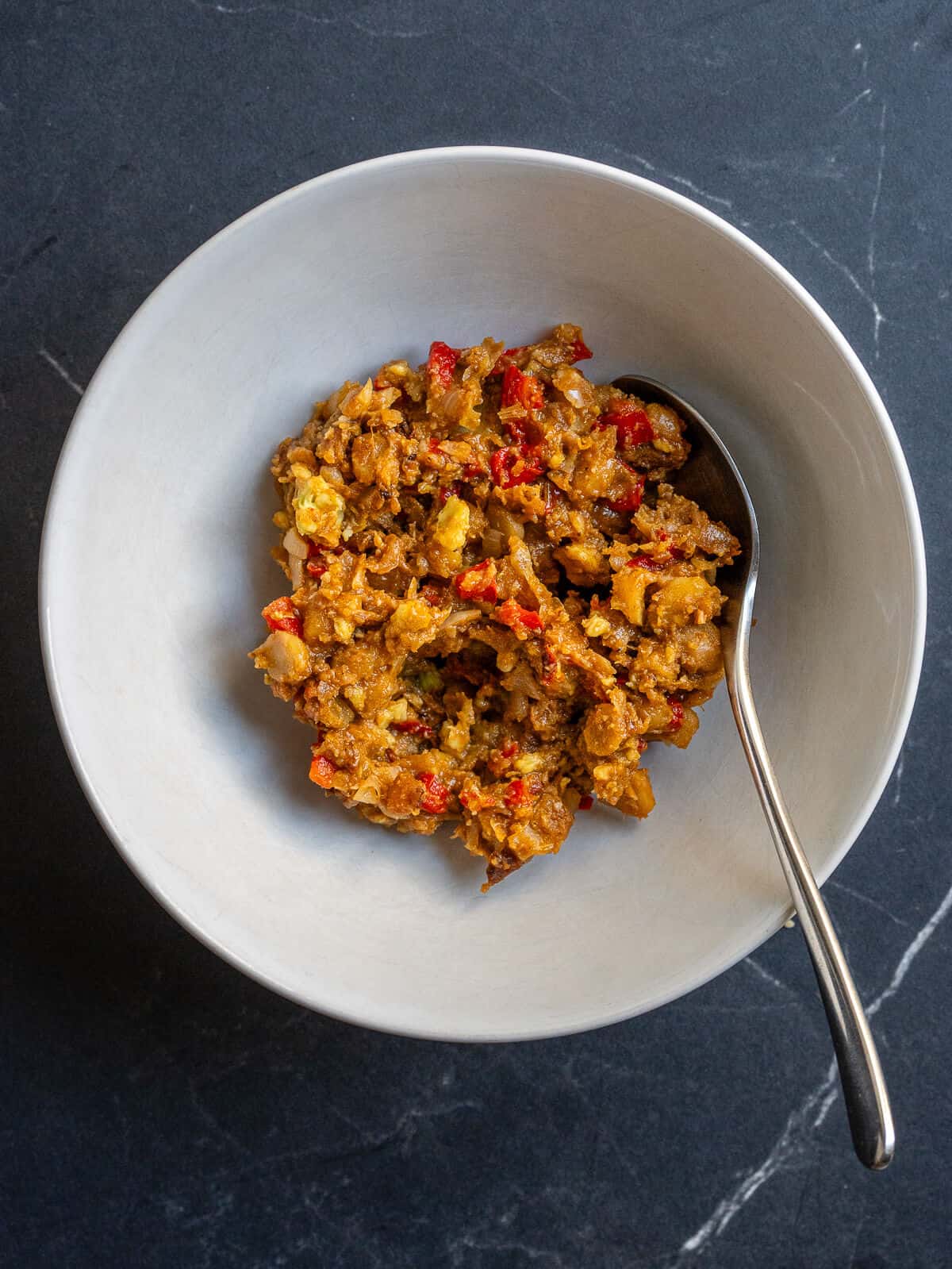 Mezcla de garbanzos machacados con pimiento, cebolleta y especias en un bol con una cuchara.