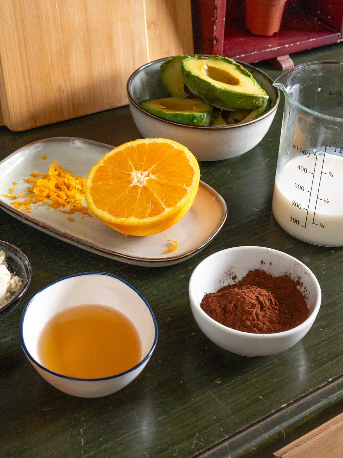 Ingredientes principales para un mousse de chocolate vegano: aguacate, cacao en polvo, leche de almendras y zumo de naranja, listos para procesar.