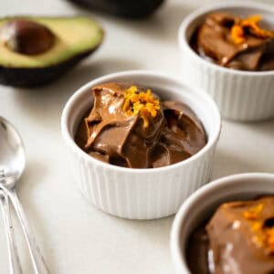 Mousse de chocolate con aguacate servido en ramequines blancos, decorado con ralladura de naranja, postre vegano cremoso y saludable.