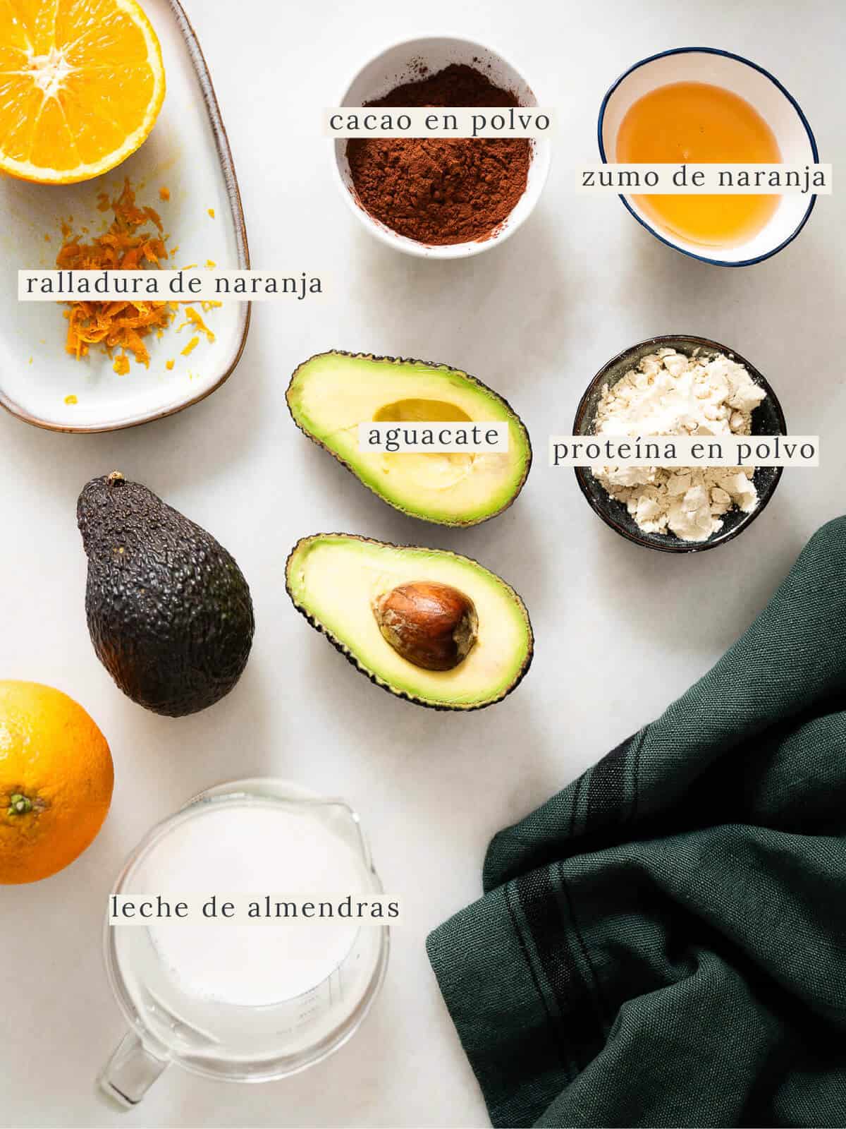 Ingredientes frescos para preparar un mousse de chocolate saludable: aguacate, cacao en polvo, naranja y leche de almendras.