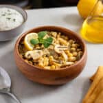 Cocido de garbanzos con verduras en un tazón rústico, decorado con limón y hojas verdes, servido con arroz.