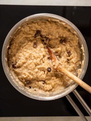 Arroz cremoso al cardamomo en proceso de cocción, con pasas y especias integradas, removido con una cuchara de madera.