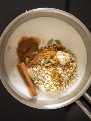 Olla con leche de coco, arroz, especias y azúcar de coco antes de cocinar, con una rama de canela y vainas de cardamomo visibles.