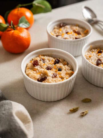 Tres porciones de arroz cremoso en ramequines blancos con pasas y especias, con mandarinas de fondo.