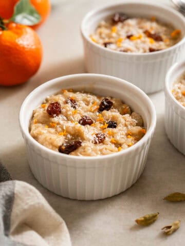 Dos ramequines con postre de arroz cremoso al cardamomo, acompañados de mandarinas frescas y semillas de cardamomo sobre una mesa.