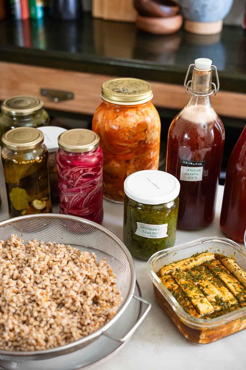 Mesa de cocina con fermentos caseros en frascos de vidrio, tofu marinado y legumbres cocidas, como parte de una dieta antiinflamatoria casera.