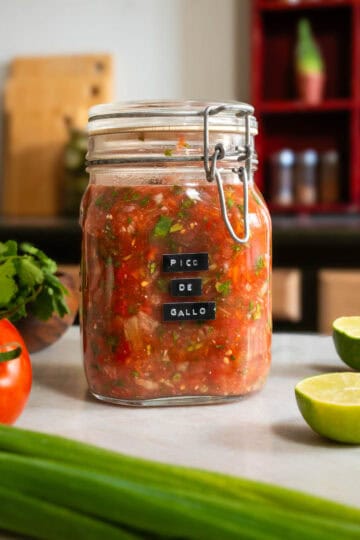 Frasco de vidrio lleno de pico de gallo casero recién preparado, con tomates, cebolla, cilantro y lima.