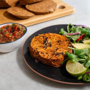 Filete de seitán casero dorado servido con ensalada de hojas verdes, aguacate y lima. Receta vegana rica en proteína vegetal, ideal como alternativa sin carne para comidas principales.