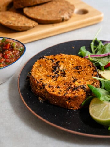Filete de seitán casero dorado servido con ensalada de hojas verdes, aguacate y lima. Receta vegana rica en proteína vegetal, ideal como alternativa sin carne para comidas principales.