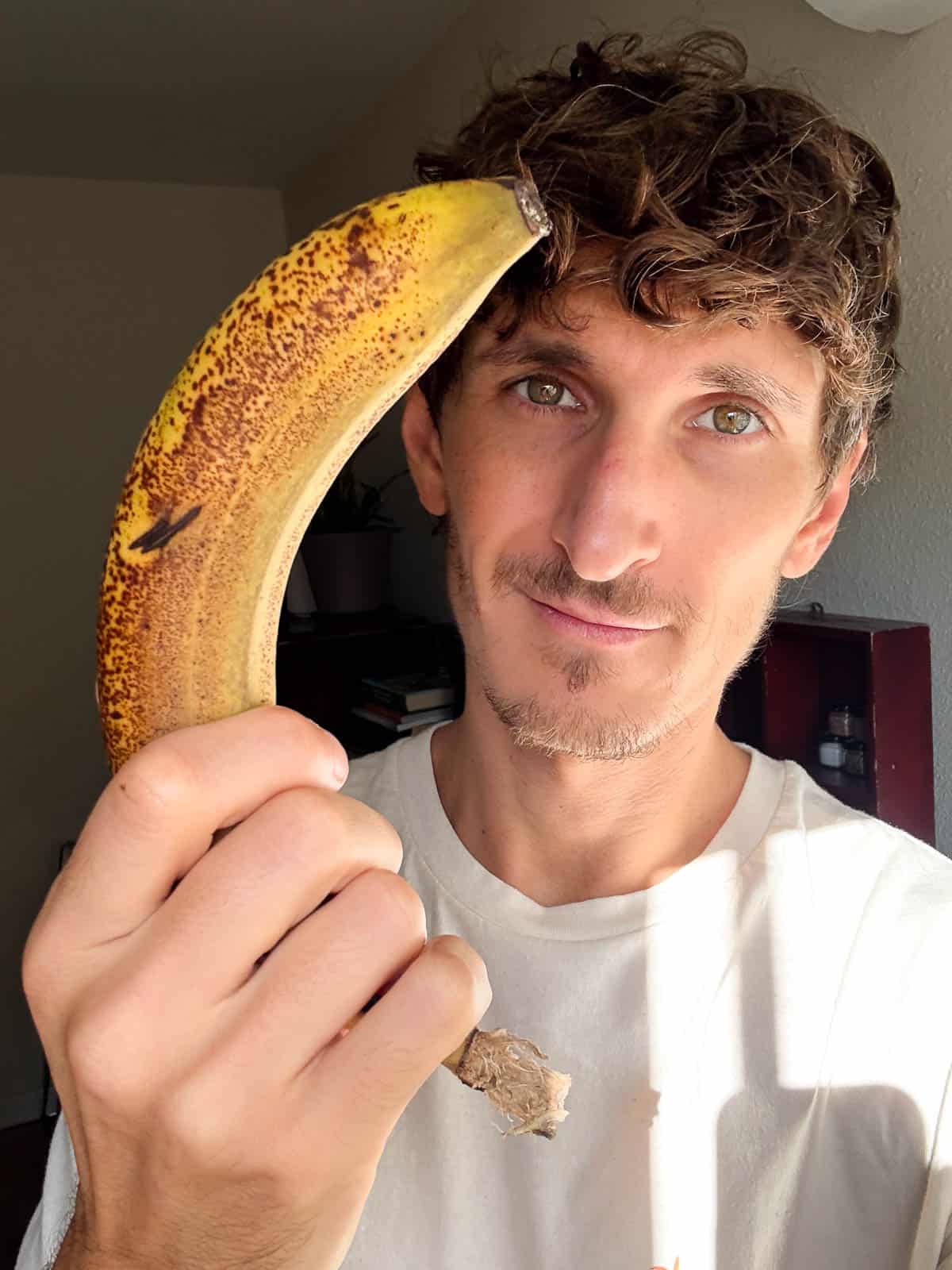 Persona sonriendo mientras sostiene un plátano maduro, listo para reutilizar su cáscara en recetas veganas.