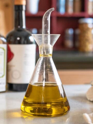 Primer plano de una aceitera de vidrio con aceite de oliva virgen extra sobre encimera de cocina.