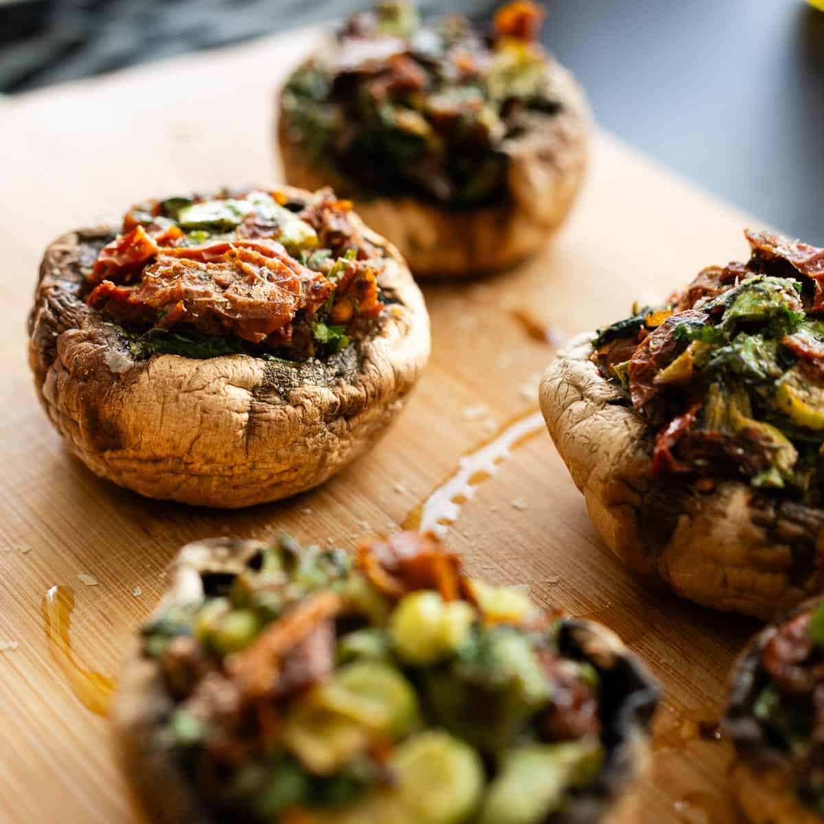 Portobellos rellenos veganos horneados, con relleno de verduras frescas y tomates secos sobre tabla de madera.