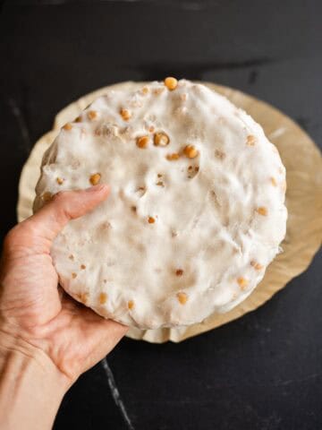 Disco de tempeh de garbanzo fermentado, sostenido con la mano sobre papel vegetal.