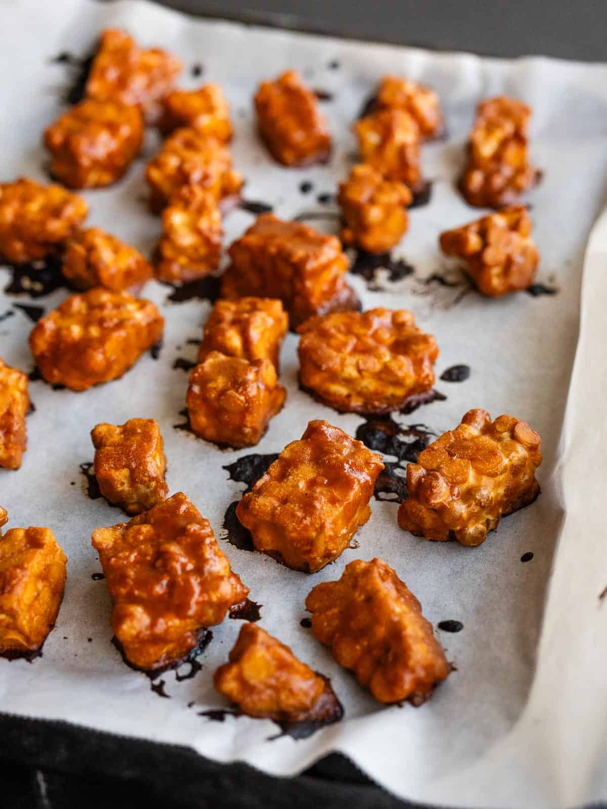 Cubos de tempeh dorados y crujientes recién salidos del horno sobre bandeja.