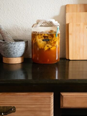 Frasco de vidrio con fermentación de piña para preparar tepache casero en casa.